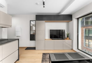 Eine moderne Küche mit integriertem Fernseher, grauen Schränken und einer Holz Arbeitsplatte.