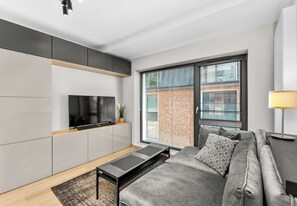 A modern living room with a sofa, TV, and a sliding glass door to a brick wall. - Main Station Comfort Studio (Kraków)