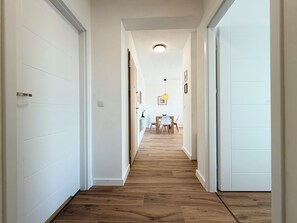 A hallway with wooden flooring, white walls, and a dining area with a table and chairs. - Wrocław Partynice Cosy Apartment (Wrocław)