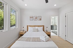 Ein modernes Schlafzimmer mit einem großen Bett, Nachttischen, einem Beistelltisch und Blick ins Bad.