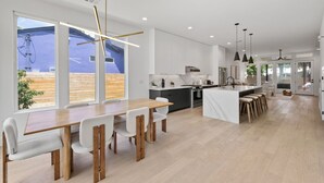 Una cocina moderna con armarios blancos, una mesa de comedor de madera e iluminación colgante.