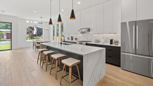 Una cocina moderna con una isla grande, taburetes de bar, iluminación colgante y electrodomésticos de acero inoxidable.