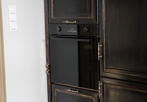 Ein schwarzer Backofen mit digitaler Uhr, die 17:41 anzeigt, ein wandmontierter Lichtschalter und eine Tür mit Messinggriff.