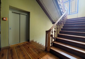 Eine Treppe mit Holzstufen und einem Holnänder, die zu einer Tür mit Lichtschalter an der Wand führt.