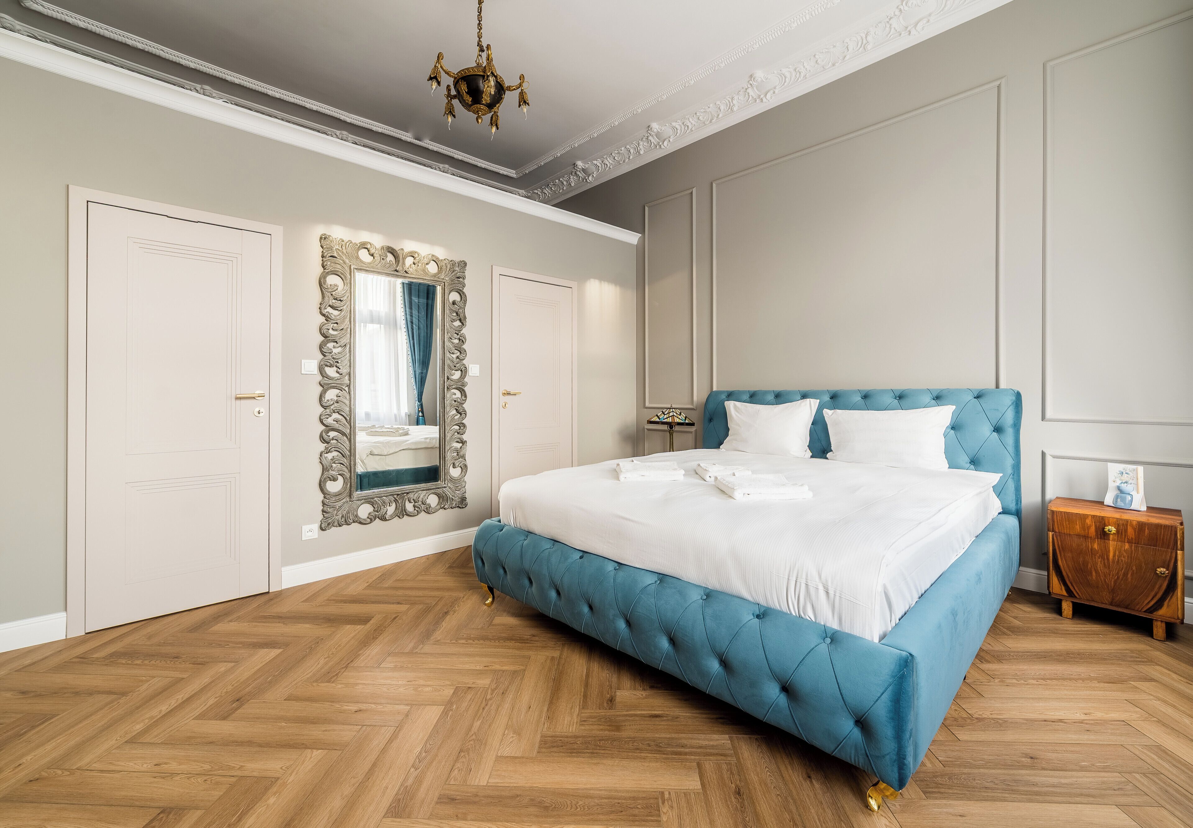 A bedroom with a large bed, a mirror, a chandelier, and a wooden floor.