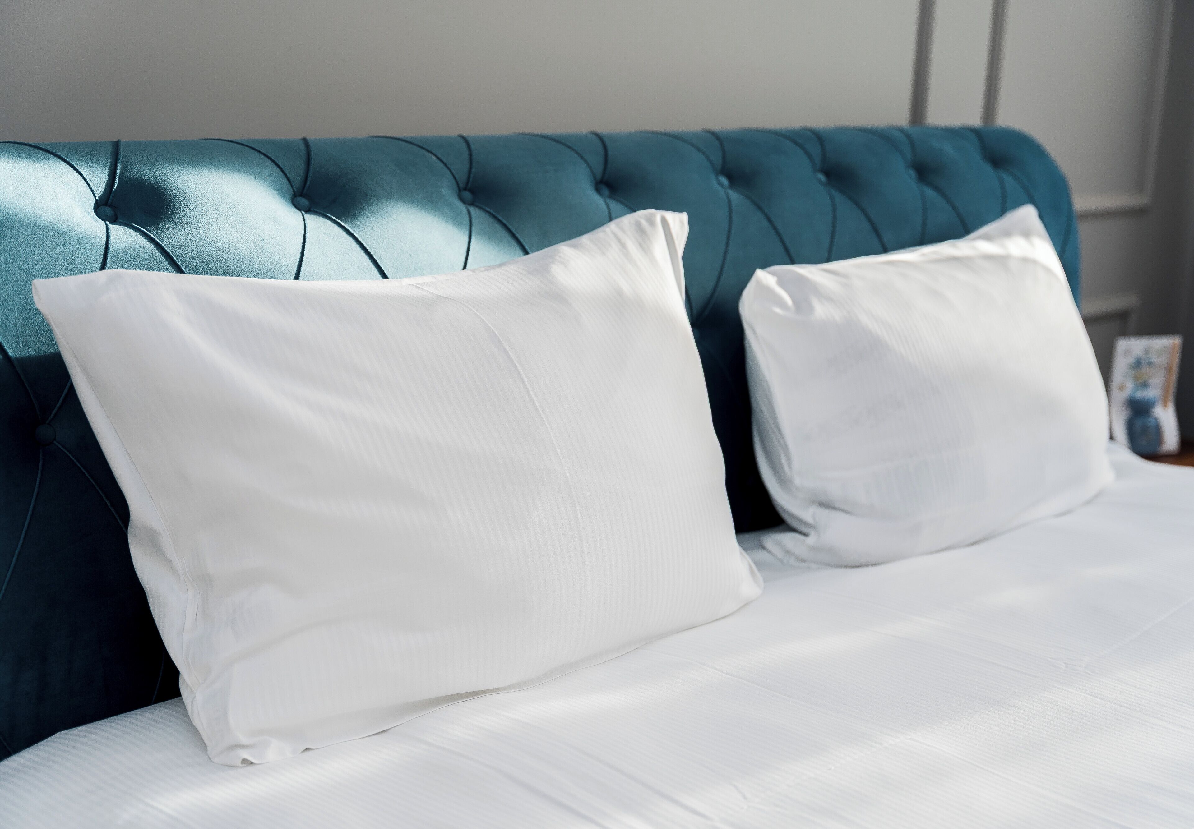 Ein Bett mit weißer Bettwäsche und einem dunkelblauen, gepolsterten Kopfteil.