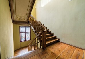 Eine Holztreppe mit verzierten Balustern, ein Fenster mit vielen kleinen Sprossen und eine schlichte Wand.