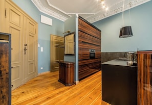 Ein Zimmer mit Holzboden, einer eingebauten Holzkabine, einer schwarzen Arbeitsplatte mit Wasserkocher und einer weißen Decke mit aufwendiger Stuckverzierung.