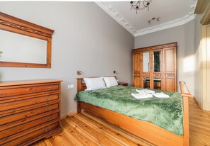 Ein Schlafzimmer mit einem Holzkapuzen, einem Bett mit grüner Decke, einem Holzschrank und einem Spiegel an der Wand.