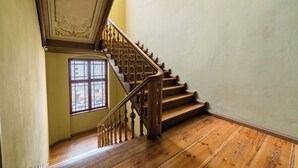 Una escalera de madera con barandillas ornamentadas, un ventanal de múltiples vidrios y una pared lisa.