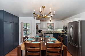 A modern kitchen with a dining table, chairs, a chandelier, cabinets, and a refrigerator. - Home in Big Bear Lake. Walk to Snow Summit, new spa, arcade, fun yard, fire pit (Big Bear Lake)