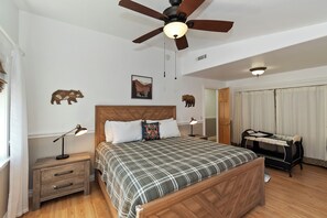 Ein Schlafzimmer mit Bett, Nachttischen, Deckenventilator, Babybett und Wanddekorationen.