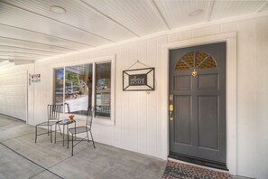 A house exterior with a garage door, a welcome sign, a dark front door, and a small patio with chairs and a table. - Home in Big Bear Lake. Walk to Snow Summit, new spa, arcade, fun yard, fire pit (Big Bear Lake)