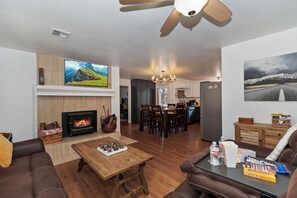 A living room with a fireplace, a dining area, and a kitchen in the background. - Home in Big Bear Lake. Walk to Snow Summit, new spa, arcade, fun yard, fire pit (Big Bear Lake)