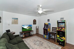 Ein Wohnzimmer mit Deckenventilator, Fernseher, Bücherregal und zwei Spielautomaten.