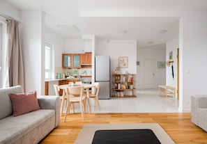 Un salon moderne comprenant un canapé, une table à manger avec des chaises, un coin cuisine avec des placards et des appareils électroménagers, et une bibliothèque.