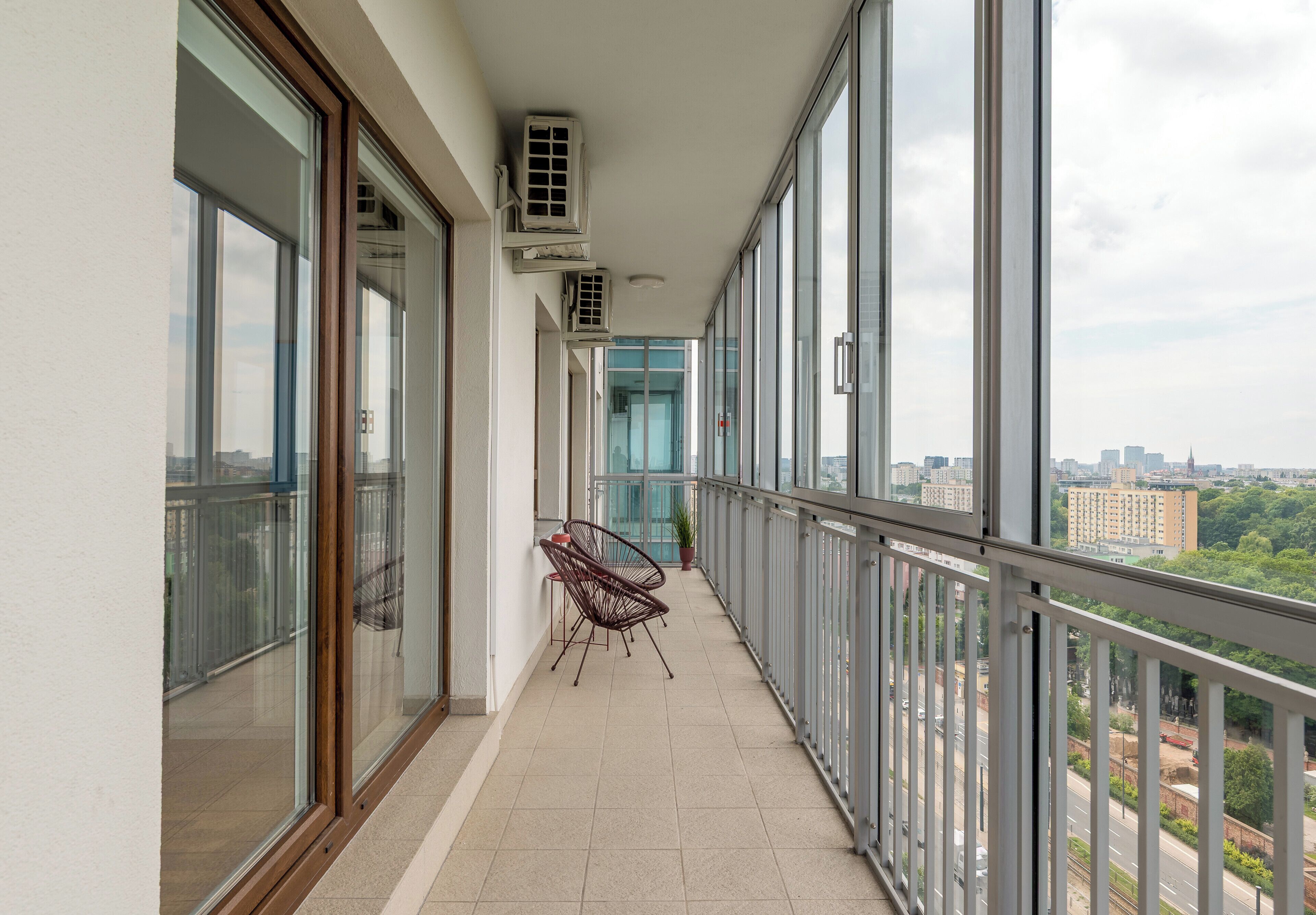 A balcony with a chair, air conditioning units, and a view of the cityscape.