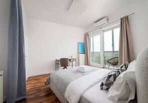 Une chambre à coucher comprenant un lit, un bureau, une chaise, une fenêtre avec des rideaux et un appareil de climatisation.