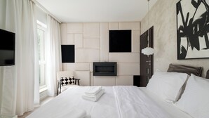 Ein Hotelzimmer mit Bett, Wandfernseher, Fenster mit Vorhängen und einem Bild an der Wand.
