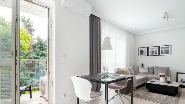 Ein modernes Wohnzimmer mit einem Glastisch, weißen Stühlen, einem grauen Sofa und einem schwarzen Couchtisch.