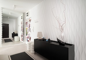 Een moderne kamer met een zwarte console tafel, een witte wand met textuur en een spiegel met verlichting.