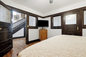 A bedroom with a large bed, a wooden dresser, a television, and a staircase.