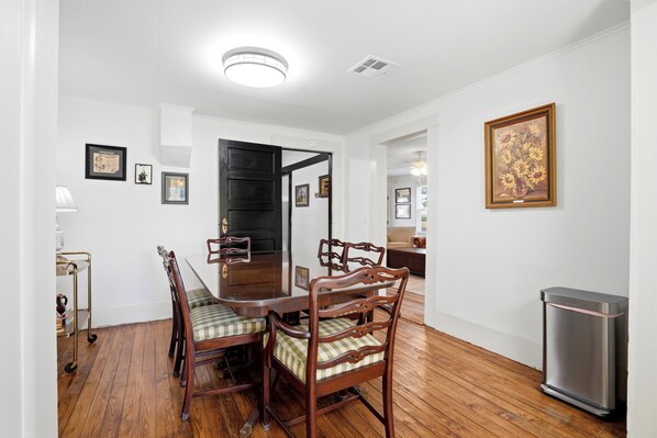 A dining area with a wooden table and chairs, a trash bin, and framed pictures on the walls.