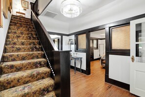 A staircase with floral carpet, a chandelier, and a door leading to a room with a white radiator.