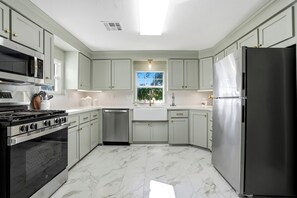 A kitchen with light green cabinets, a stainless steel refrigerator, a built-in oven, and a dishwasher.