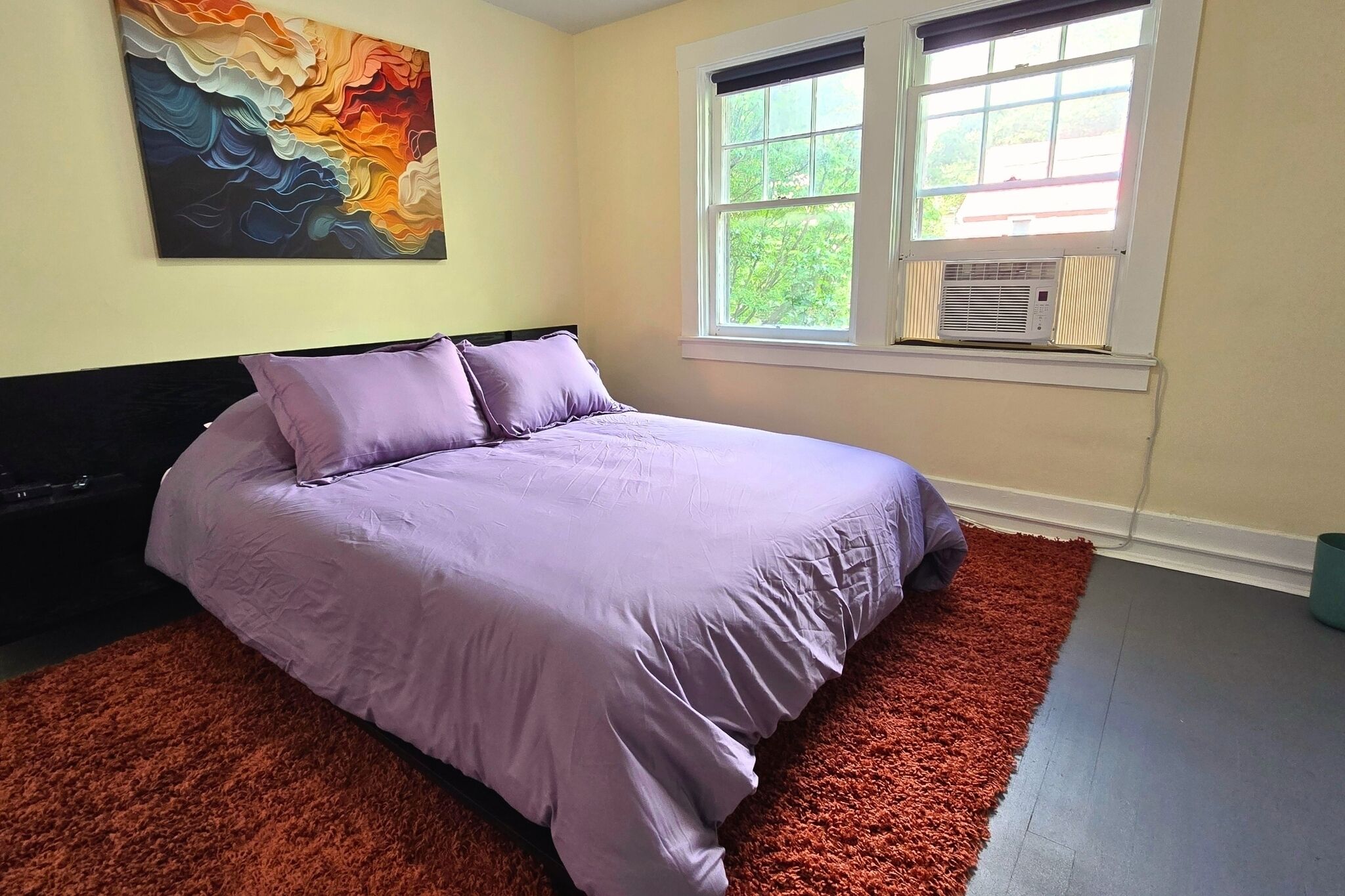 Bright cozy bedroom with lavender bedding, bold art, and natural light