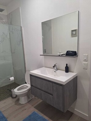 Ein modernes Badezimmer mit einem weißen Waschbecken, einem Spiegel darüber und einer Toilette links.