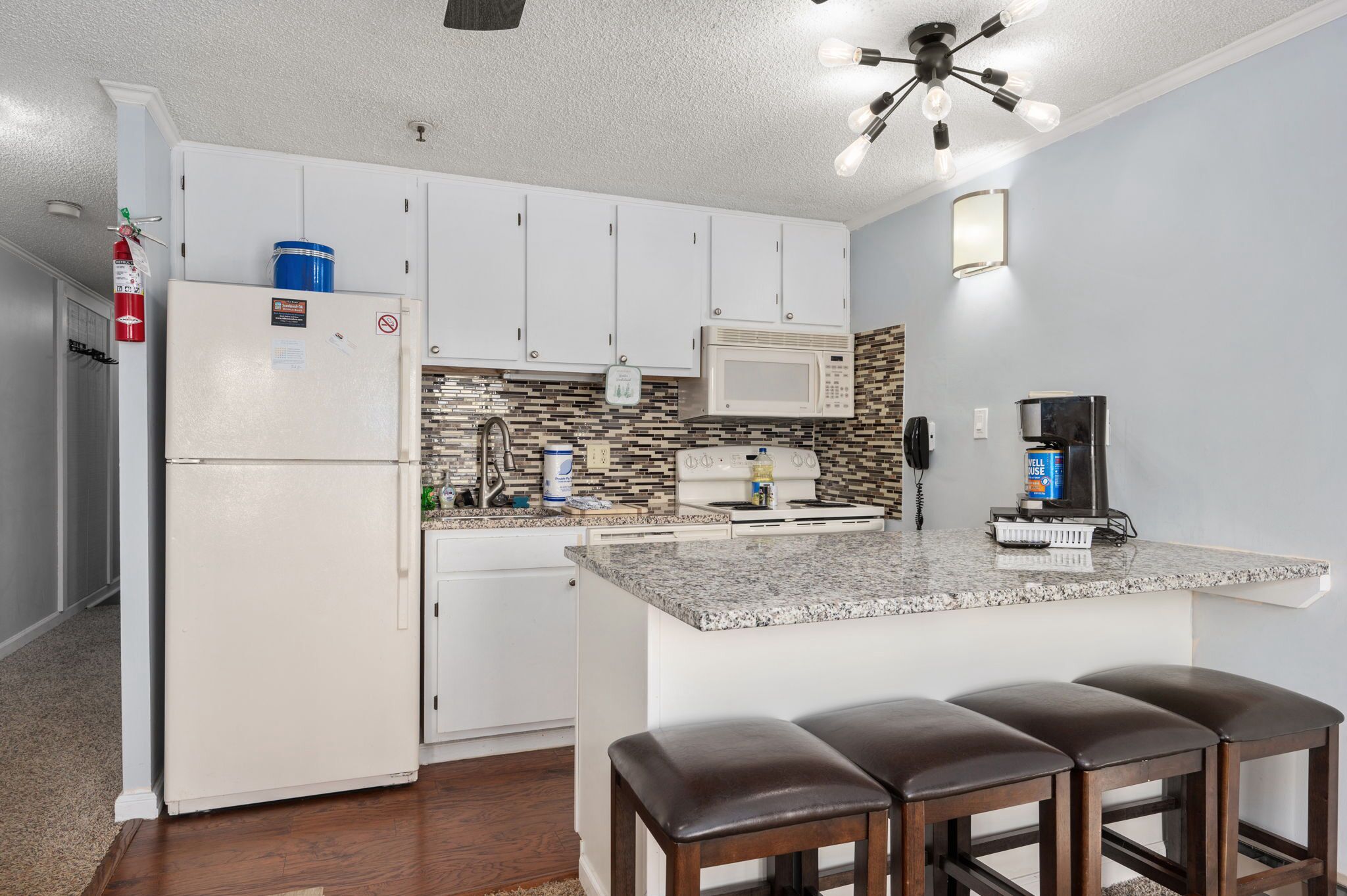 A kitchen with white cabinets, a granite countertop, a microwave, and a coffee maker.