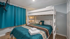 Une chambre avec un lit superposé, une couvre-lit turquoise, une serviette blanche pliée sur le lit du bas et une fenêtre avec des rideaux turquoise.