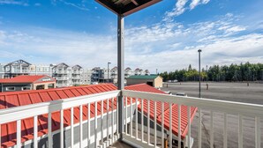 Un balcon offrant une vue sur une rangée d’immeubles aux toits rouges, un parking et une forêt en arrière-plan.