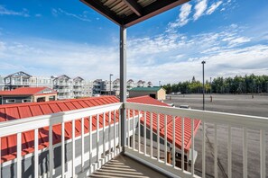 Ein Balkon mit Blick auf eine Häuserreihe mit roten Dächern, einen Parkplatz und einen Wald im Hintergrund.