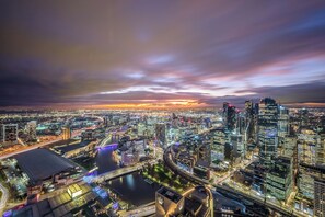 A cityscape at dusk with illuminated buildings and a river. - Exclusive Stays - Prima Penthouse (Southbank)