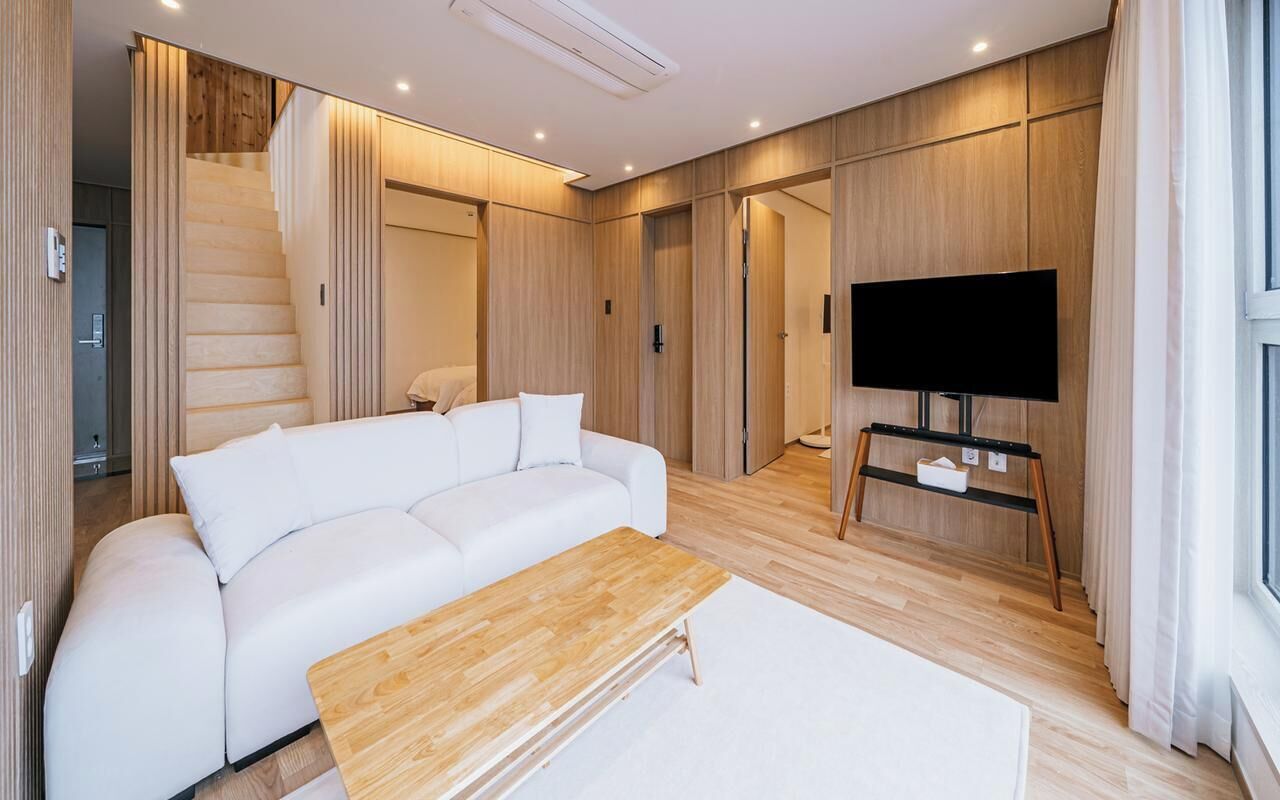 A modern living room with a white sofa, a wooden coffee table, a flat-screen TV, and a staircase.
