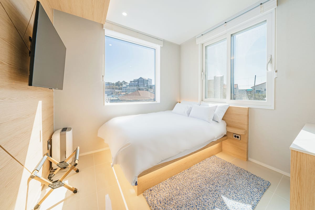 Une chambre à coucher moderne avec un lit, de grandes fenêtres et un téléviseur fixé au mur.