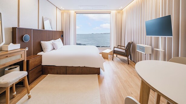 Una habitación de hotel moderna con una cama grande, un escritorio, una silla, un televisor y vistas al mar.