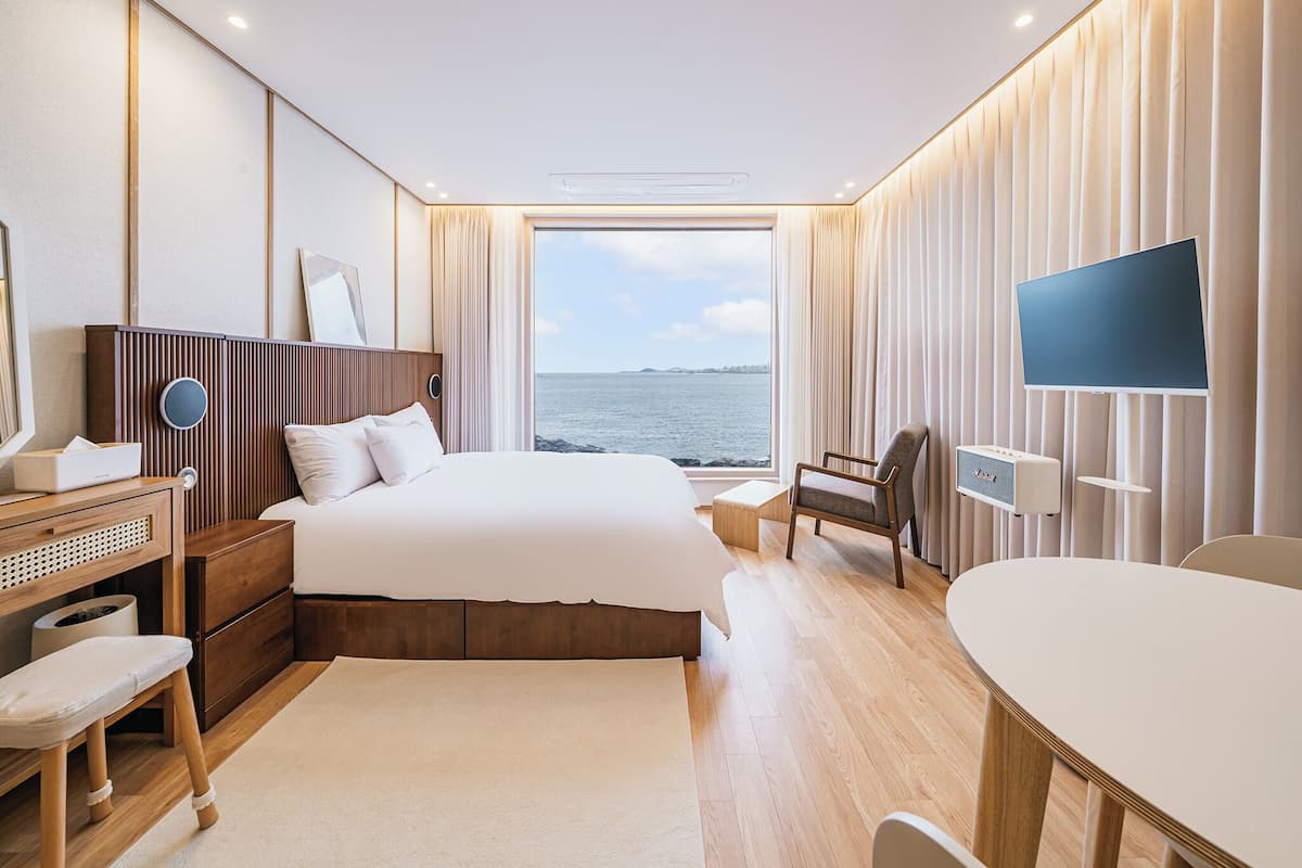 Une chambre d’hôtel moderne dotée d’un grand lit, d’un bureau, d’une chaise, d’une télévision et offrant une vue sur la mer.