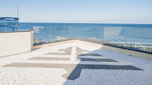 Terraço no telhado com vista clara para o mar, guarda-corpo de vidro e piso com padrão de pedrinhas.