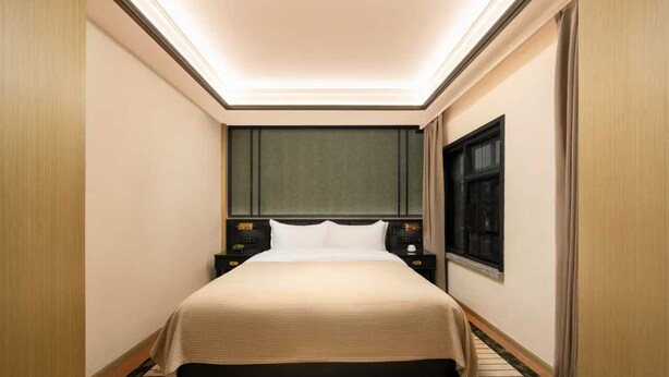 A hotel room with a bed, a nightstand, a window, and a door.