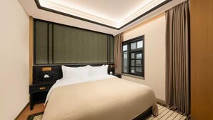 A hotel room with a large bed, a nightstand, a window, and a curtain.