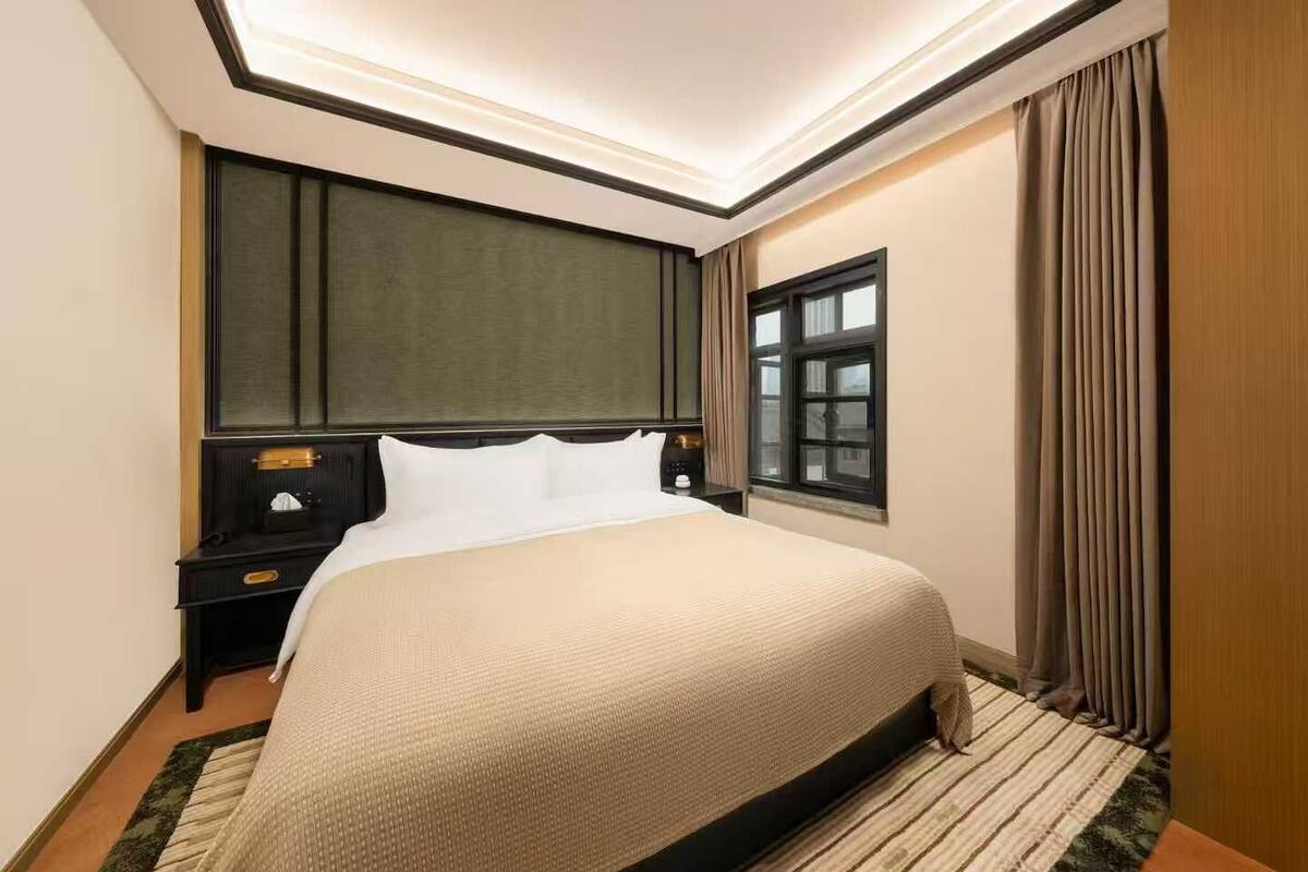 A hotel room with a large bed, a nightstand, a window, and a curtain.