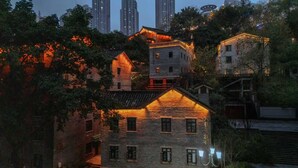 A traditional building with multiple windows and a sloped roof, surrounded by trees and modern high-rise buildings in the background.