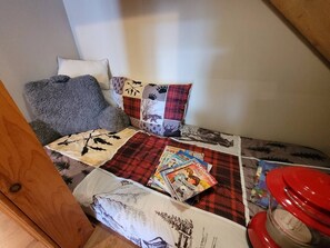 Ein kleiner, gemütlicher Raum mit einem Bett, Kissen, einer Steudecke und einem roten Behälter.