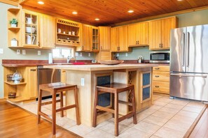 Eine Küche mit Holzschränken, einem Edelstahlkühlschrank, einer Spüle und Barhocker.