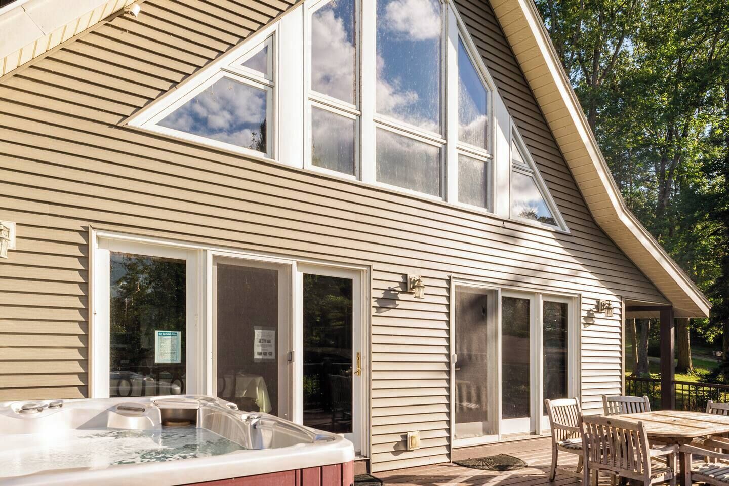 A house with a large deck, a hot tub, and a covered patio area.