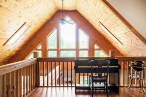 Ein Dachzimmer aus Holz mit Klavier, Stuhl, Teleskop und einem Balkongeländer.