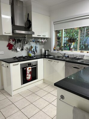 A modern kitchen with white cabinets, a black countertop, and a stainless steel range hood. - Light bright and airy, garden outlook from every window, quiet location (Glen Iris)